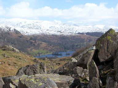 A rocky hillside overlooking a lake with snow-covered mountains in the background at Maple - Woodland Cottages in Bowness-on-Windermere