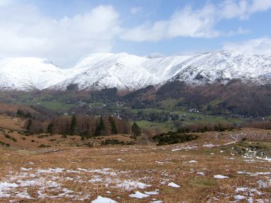 A landscape view of snow covered mountains with patches of snow on grassy fields at Maple - Woodland Cottages in Bowness-on-Windermere