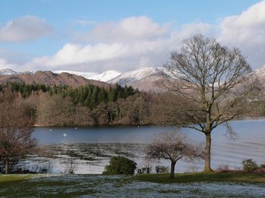 A lake with trees and snow-covered mountains in the background at Maple - Woodland Cottages in Bowness-on-Windermere
