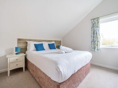 A bedroom with a bed bedside table and window at Maple - Woodland Cottages in Bowness-on-Windermere