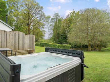 A hot tub in a grassy backyard with trees and a wooden fence at Maple - Woodland Cottages in Bowness-on-Windermere
