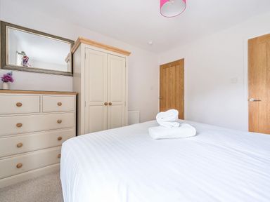 A bedroom with a bed with folded towels a chest of drawers with a mirror and a wardrobe at Maple - Woodland Cottages in Bowness-on-Windermere