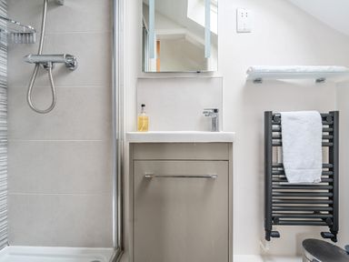 A bathroom with a shower, sink, mirror, towel rack with a towel, and a shelf with a towel at Maple - Woodland Cottages in Bowness-on-Windermere