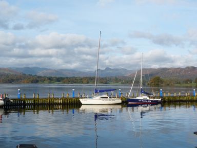 Two sailboats moored at a wooden dock on a calm lake with mountains in the background at Acorn in Bowness-on-Windermere