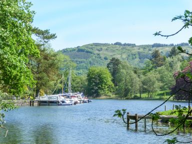 A lake with boats moored at a dock surrounded by trees and hills at Acorn in Bowness-on-Windermere