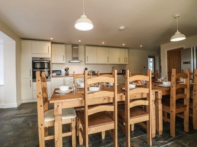 A kitchen with wooden dining table and chairs set with dishes and glasses at Rhos Helyg in Penysarn near Amlwch