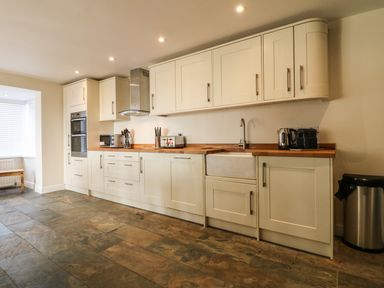 A kitchen with wooden countertops white cabinets built in oven a sink and appliances at Rhos Helyg Penysarn near Amlwch