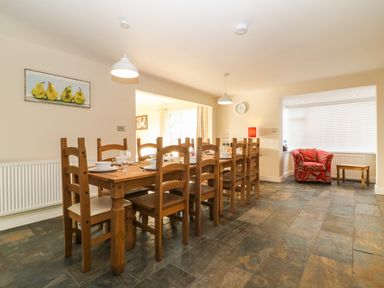 A dining room with a long wooden table set with dishes and glasses and wooden chairs at Rhos Helyg in Penysarn near Amlwch