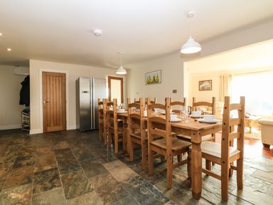 A dining room with a long wooden table and chairs set with dishes and glasses at Rhos Helyg in Penysarn near Amlwch