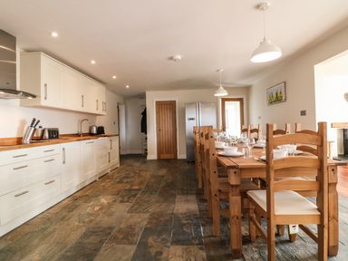 A kitchen with white cabinets a wooden dining table with chairs and a refrigerator at Rhos Helyg in Penysarn near Amlwch