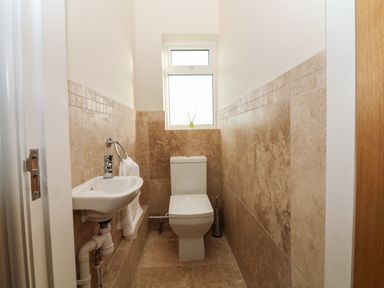 A narrow bathroom with a toilet and a small wall-mounted sink near a window at Rhos Helyg in Penysarn near Amlwch