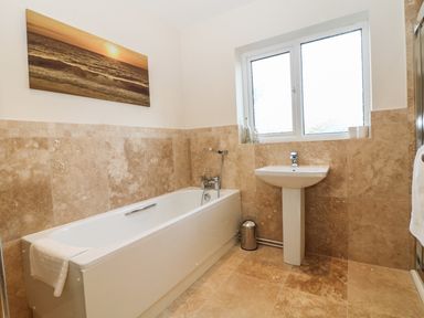 A bathroom with a bathtub a pedestal sink a window and a wall painting of a sunset at Rhos Helyg in Penysarn near Amlwch