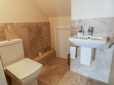A bathroom with a toilet and a wall-mounted sink with beige tiled walls and floor at Rhos Helyg in Penysarn near Amlwch