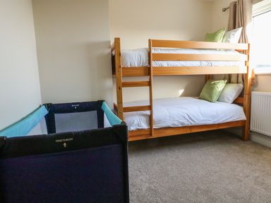 A bedroom with a wooden bunk bed and a blue portable crib near a window at Rhos Helyg in Penysarn near Amlwch