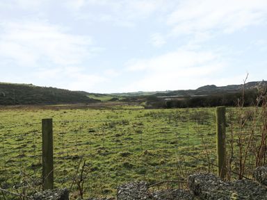 A green grassy field with a wire fence in the foreground and hills in the background at Rhos Helyg in Penysarn near Amlwch