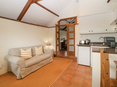A living room with a beige sofa and striped cushions next to a small kitchen with white cabinets and wooden furniture at Nestling Barn in Peter Tavy near Tavistock
