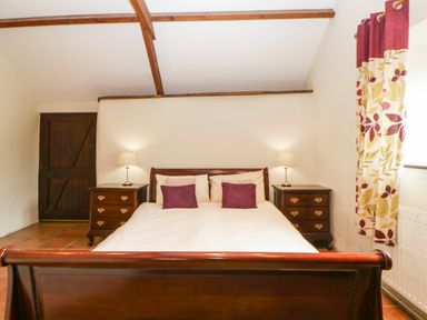 A bedroom with a wooden double bed two bedside tables with lamps and a window with floral curtains at Nestling Barn Peter Tavy near Tavistock