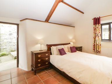 A bedroom with a double bed two bedside tables with lamps tiled floor and a window with patterned curtains at Nestling Barn Peter Tavy near Tavistock
