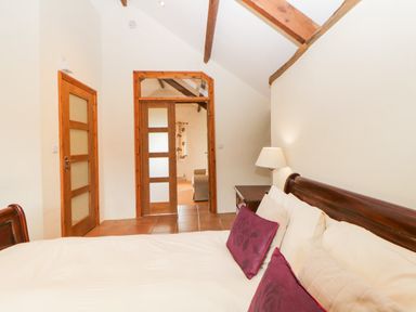 A bedroom with a wooden bed frame purple and cream pillows a bedside table with a lamp and wooden doors at Nestling Barn Peter Tavy near Tavistock