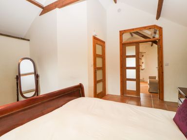 A bedroom with a wooden bed frame a full length mirror and wooden doors leading to another room at Nestling Barn Peter Tavy near Tavistock