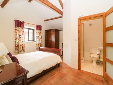 A bedroom with a bed curtains wooden furniture and an en suite bathroom at Nestling Barn in Peter Tavy near Tavistock