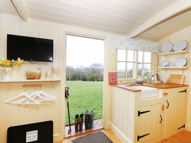 A small kitchen with wooden countertops and a sink next to an open door showing a grassy field at Bramble Burlawn near Wadebridge