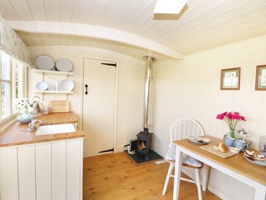 A small kitchen with wooden countertop sink wood stove and a table with chairs and flowers at Bramble Burlawn near Wadebridge