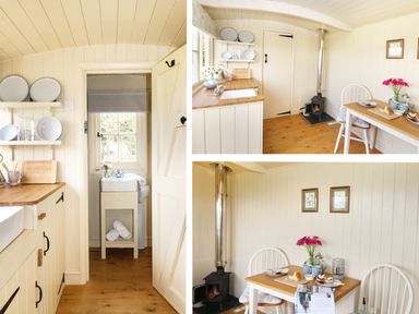 A kitchen area with wooden countertops, shelves with dishes, a small stove, and a dining table with two chairs and flowers at Bramble Burlawn near Wadebridge
