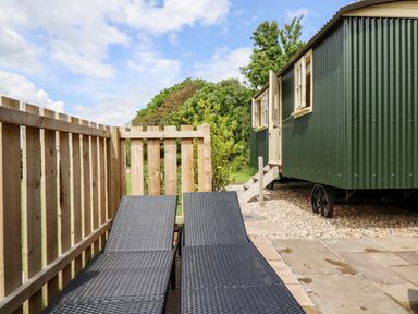 An outdoor area with two black lounge chairs next to a wooden fence and a green corrugated metal cabin with open windows at Bramble Burlawn near Wadebridge