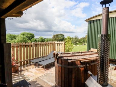 An outdoor patio area with wooden hot tub chimney two lounge chairs wooden fence and green corrugated building at Bramble Burlawn near Wadebridge