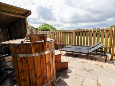An outdoor patio with a wooden hot tub and two black lounge chairs near a wooden fence at Bramble Burlawn near Wadebridge