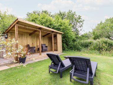 A garden with two loungers and a wooden sheltered seating area at Willow Burlawn near Wadebridge