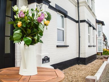 A vase with flowers on a wooden table outside a white brick house at Oak Lodge East Runton