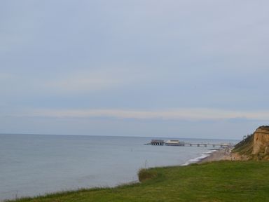A coastline view with a grassy cliff overlooking the sea and a pier extending into the water at Oak Lodge in East Runton