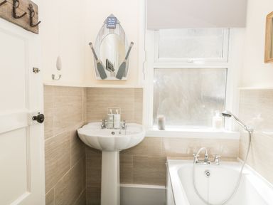 A bathroom with a pedestal sink a bathtub with handheld shower and a window at Oak Lodge in East Runton