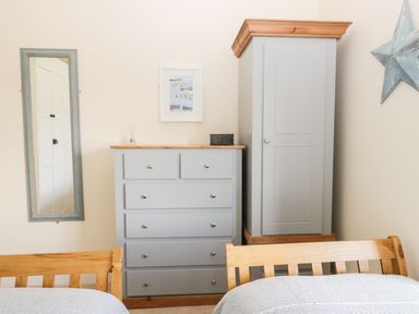 A bedroom corner with two wooden beds a gray dresser with drawers and cabinet a wall mirror and a star decoration at Oak Lodge East Runton