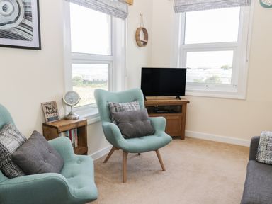 A living room with two armchairs a small wooden side table a television on a wooden stand and windows at Oak Lodge in East Runton