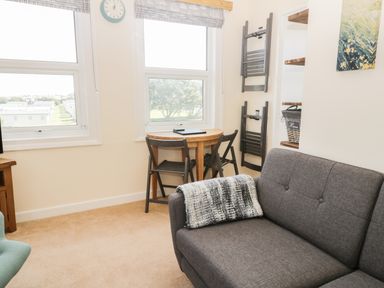 A small living room with a gray sofa a round wooden table with two chairs and two windows at Oak Lodge in East Runton
