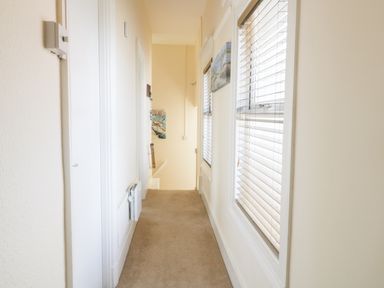 A narrow hallway with beige carpet white walls stairs at the end and windows with blinds on the right at Oak Lodge in East Runton