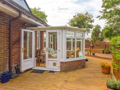 A wooden deck leading to a conservatory with open doors and potted plants on the side at Estuary View in Warkworth