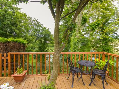 A wooden deck with a metal table and two chairs surrounded by trees and plants at Estuary View in Warkworth