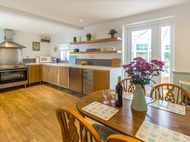 A kitchen with wooden cabinets a dining table with flowers and wine near glass doors at Estuary View in Warkworth
