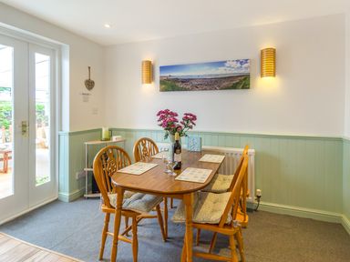 A dining area with a wooden table and four chairs with seat cushions and placemats flowers in a vase and a bottle on the table at Estuary View in Warkworth