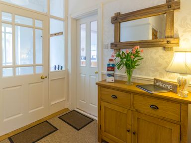 An entryway with wooden cabinet holding flowers lamp and welcome sign and glass paneled doors at Estuary View in Warkworth