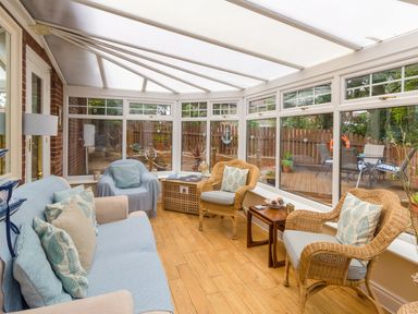 A conservatory with wicker chairs a sofa and a wooden floor at Estuary View in Warkworth