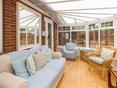 A conservatory with a sofa chair wicker chair and wooden floor at Estuary View in Warkworth