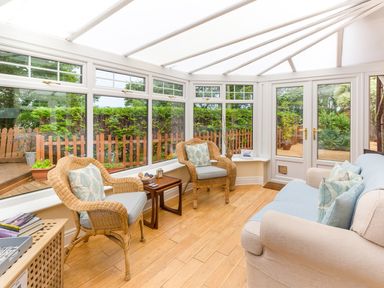 A conservatory with wicker chairs sofa and wooden floor at Estuary View in Warkworth