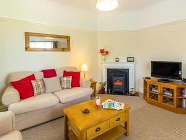 A living room with beige sofa with red and plaid cushions a wooden coffee table a fireplace and a TV on a wooden cabinet at Estuary View in Warkworth