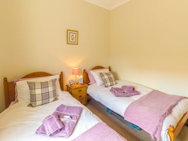A bedroom with two single beds with pink towels and a wooden nightstand with a lamp at Estuary View in Warkworth