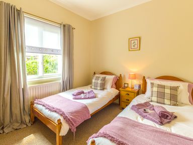 A bedroom with two single beds a window with curtains and a bedside table with a lamp at Estuary View in Warkworth